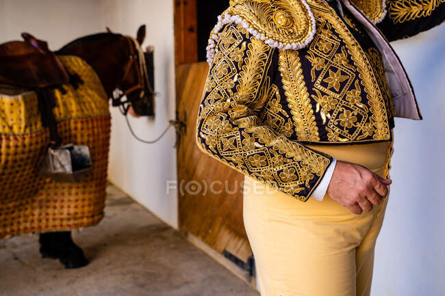 Crop anonymous picador wearing traditional shiny costume standing next to horse — Stock Photo