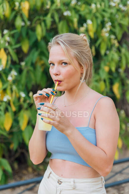 Чарівна жінка п'є холодний освіжаючий лимонад з соломою під час охолодження в літньому саду і дивлячись на камеру — стокове фото