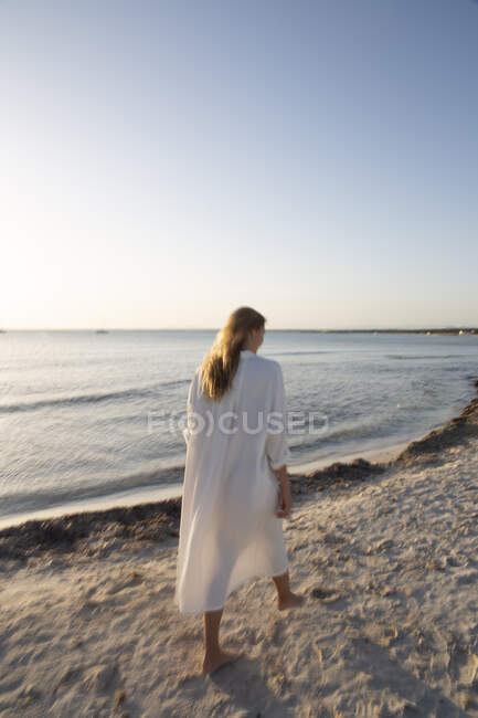 Длинноволосая блондинка, стоящая на пляже и смотрящая вдаль — стоковое фото