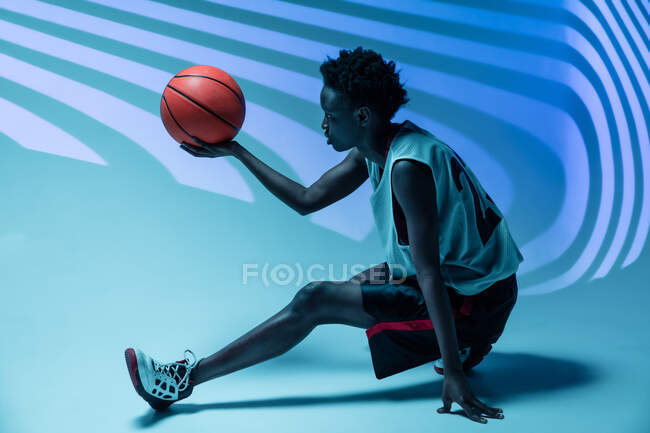 Schwarze Frau mit Basketballoutfit im Studio mit Farbgelen und Projektorlichtern vor blauem Hintergrund — Stockfoto