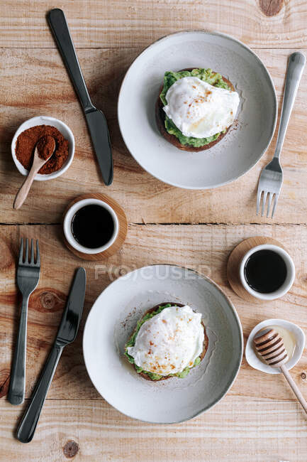 Appetitliche Scheibe Kornbrot mit Avocado und pochiertem Ei auf Platte auf Holztisch gelegt — Stockfoto