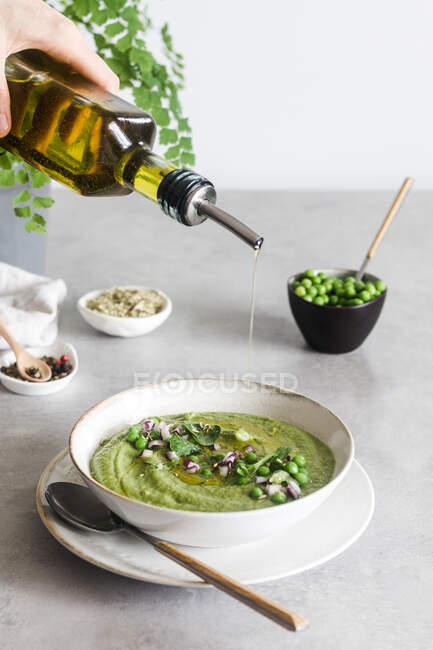 Anonyme versant de l'huile d'olive sur une délicieuse crème de pois sur une table en béton blanc — Photo de stock