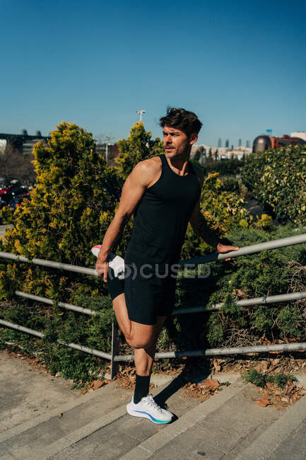 Мужской спортсмен в спортивной одежде тренируется на городской лестнице, глядя в сторону парка в солнечный день — стоковое фото