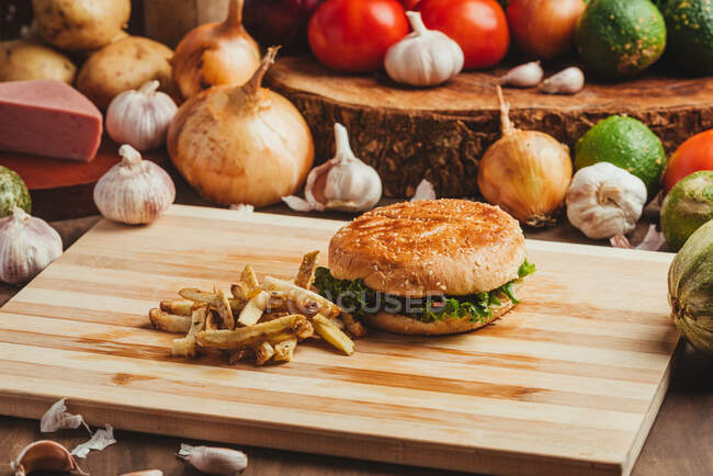 Appetizing hamburgers with vegetables placed on wooden board with French fries in kitchen — Stock Photo