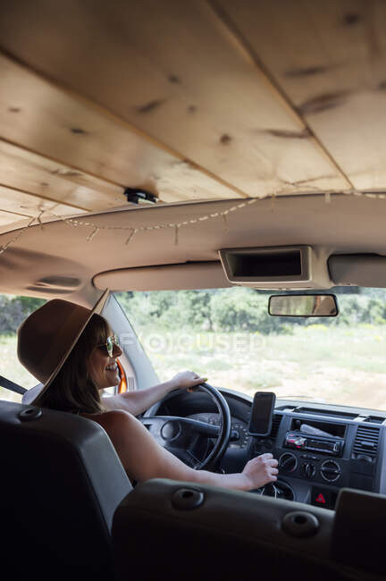 Вид сбоку женщины, сидящей на водительском сиденье в фургоне и наслаждающейся поездкой по дороге летом — стоковое фото