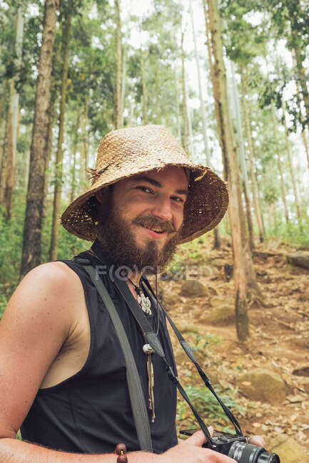 Cheerful traveling male photographer taking pictures on photo camera during summer adventure in forest — Stock Photo