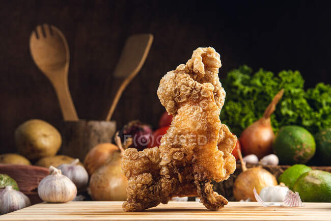 Tasty crispy fried chicken served on wooden cutting board on table with assorted vegetables in kitchen — Stock Photo