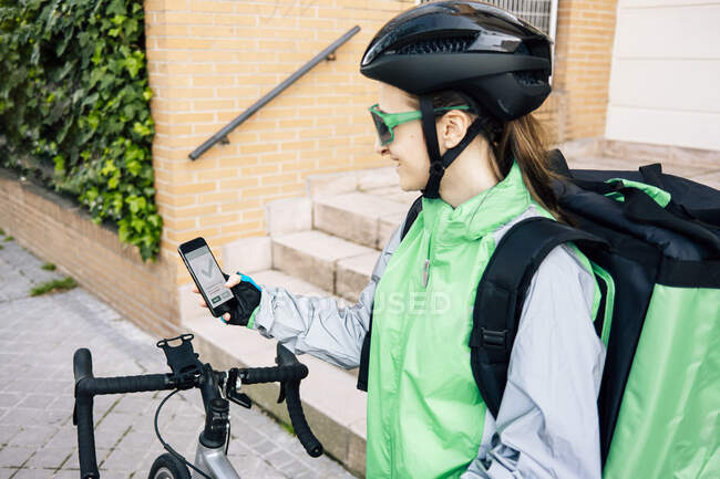 Visão traseira do correio examinando rota no mapa GPS antes de andar de bicicleta na rua da cidade — Fotografia de Stock