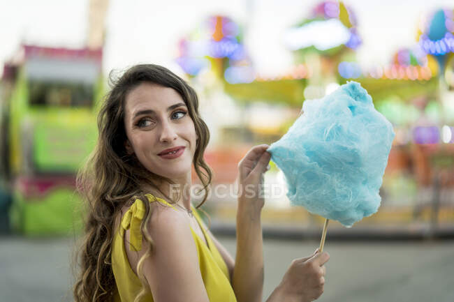 Vista lateral da mulher feliz comendo doces de algodão azul doce enquanto se diverte e desfruta de fim de semana no parque de diversões no verão — Fotografia de Stock