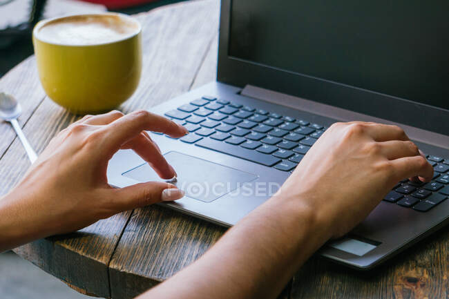 Cropped unrecognizable female freelancer typing on laptop keyboard while working on remote project on cafe terrace — Stock Photo