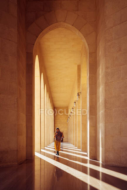 Unerkennbare Frau in traditioneller orientalischer Kleidung geht durch eine lange Bogenhalle mit Steinsäulen der berühmten Al-Fateh-Moschee in Bahrain — Stockfoto