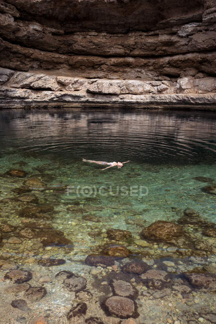 Relaxado mulher anônima flutuando em água transparente de Bimmah Sinkhole cercado por rochas ásperas durante a viagem em Omã — Fotografia de Stock