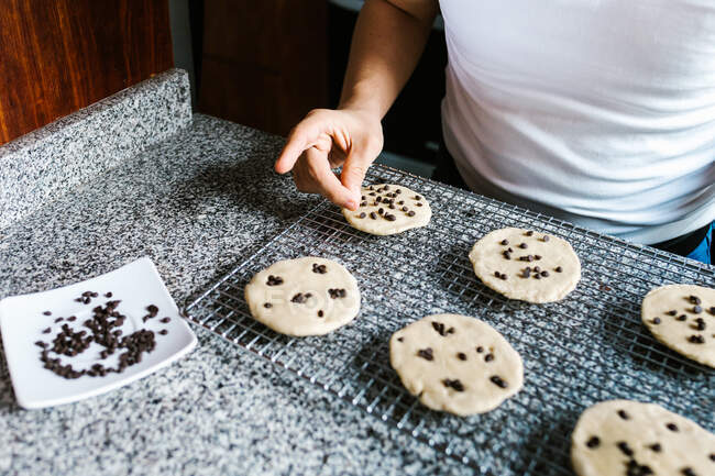 Неупізнаваний підліток, готуючи їжу вдома, прикрашає сире печиво шоколадними цукерками. — стокове фото
