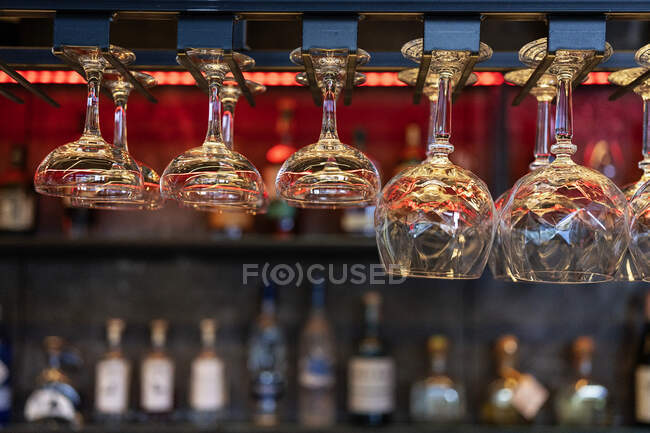Various clean crystal glasses of different shape and size hanging on shelves over counter in bar — Stock Photo
