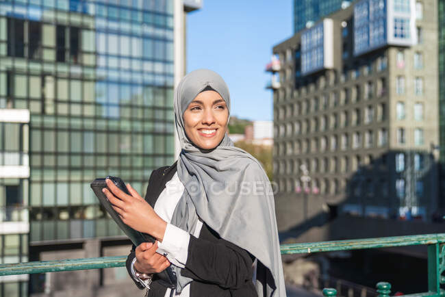 Empreendedora muçulmana alegre no hijab e com café takeaway em pé na rua — Fotografia de Stock