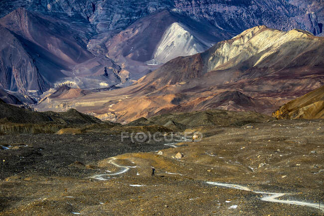 Remote view of hiker standing on rocky ground in highlands on background of rough Himalayas mountain range in Nepal — Stock Photo