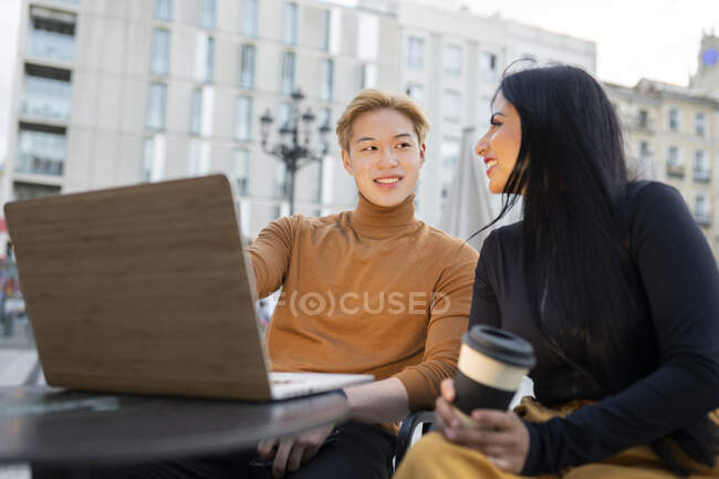 Cheerful multiracial freelancer sitting at table with laptop and working on remote project together in outdoors cafe — Stock Photo