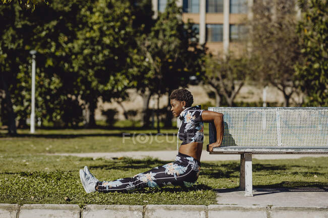 Young fitness African American woman making exercise after running on park bench — Stock Photo