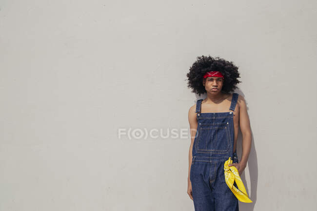 Young ethnic male in retro clothes with Afro hairstyle leaning on concrete wall while looking at camera — Stock Photo