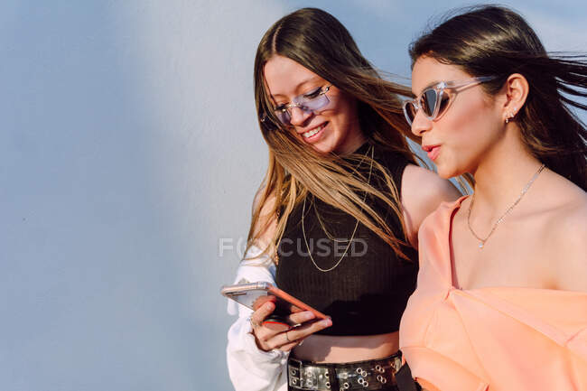 Positive female friends sharing mobile phone and surfing Internet while spending free time together — Stock Photo