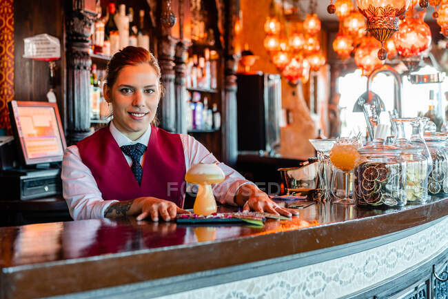 Улыбающаяся барменша, стоящая у барной стойки с алкогольным напитком, подается в креативных коктейльных бокалах в форме грибов — стоковое фото