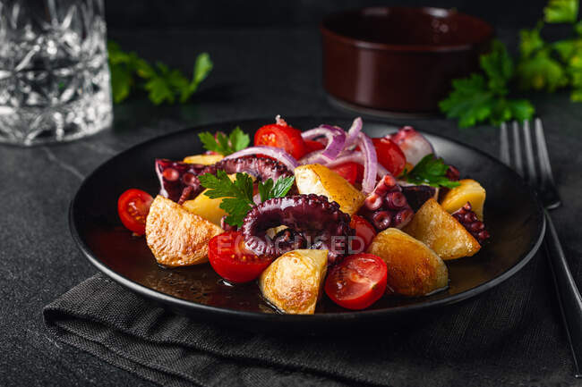 Tasty salad with octopus and assorted vegetables and herbs on plate on table — Stock Photo