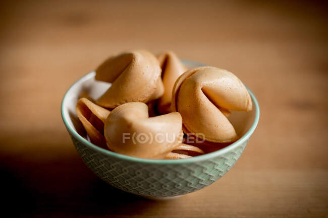 Closeup small bowl full of crispy fortune cookies placed on wooden table — Stock Photo