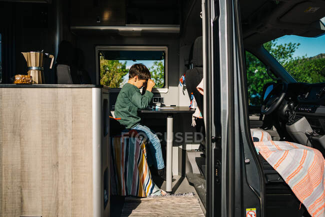 Little boy sitting inside a motorhome while doing his homework — Stock Photo