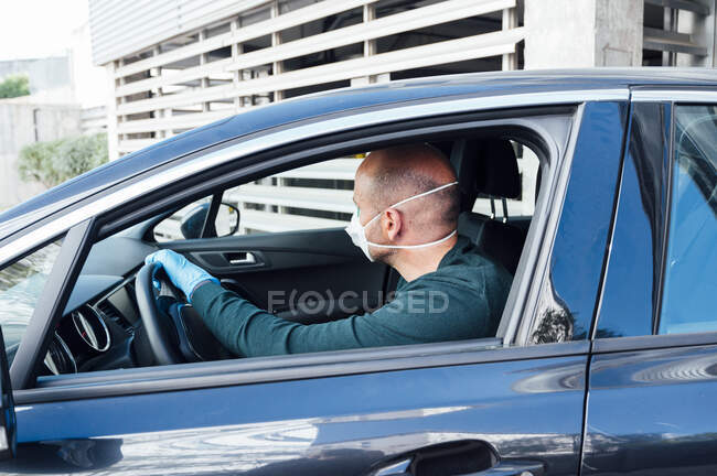 Vista lateral del hombre serio usando una máscara protectora que conduce el coche durante el tiempo de cuarentena - foto de stock