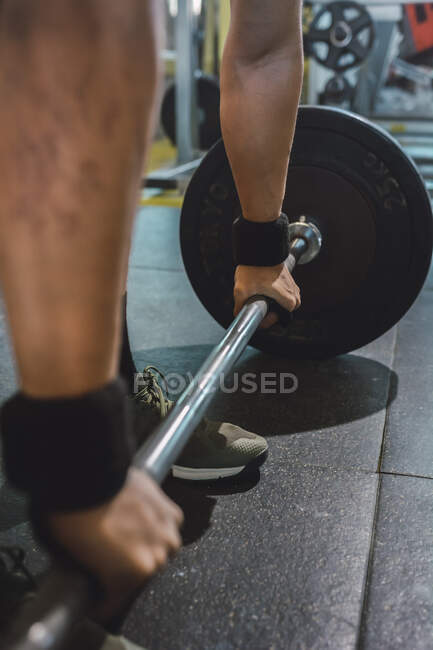 Cultivé athlète masculin méconnaissable faisant haltérophilie avec haltère lourde pendant l'entraînement dans la salle de gym — Photo de stock