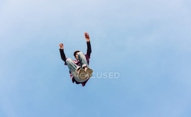Du dessous du mâle sautant au-dessus du sol et effectuant un cascade de parkour sur fond de ciel bleu sans nuages — Photo de stock
