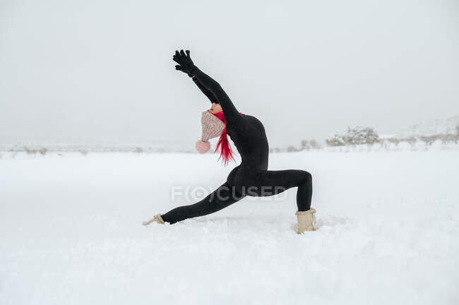 Бічний вид гнучкої самиці, яка практикує йогу в Анханеясані, стоячи на сніговому полі взимку. — стокове фото