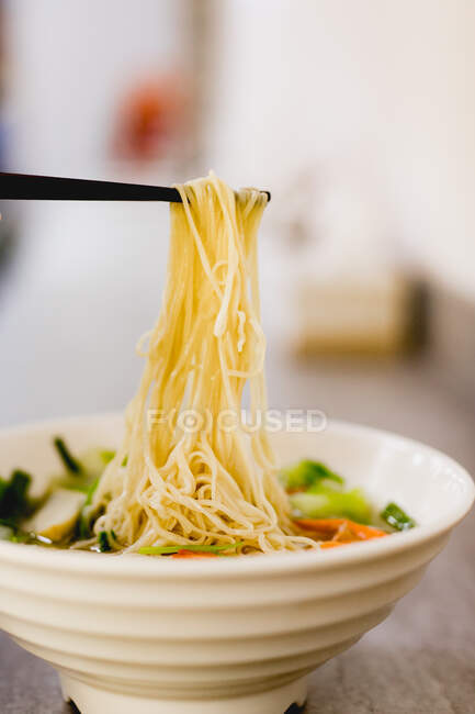 Side view of hand eating bowl of tasty seafood noodles with chopsticks on black wooden table in Asian cafe — Stock Photo