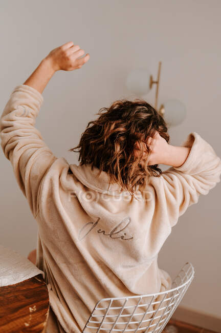 Back view of faceless tranquil female in soft bathrobe stretching on chair after sleep in morning at home — Stock Photo