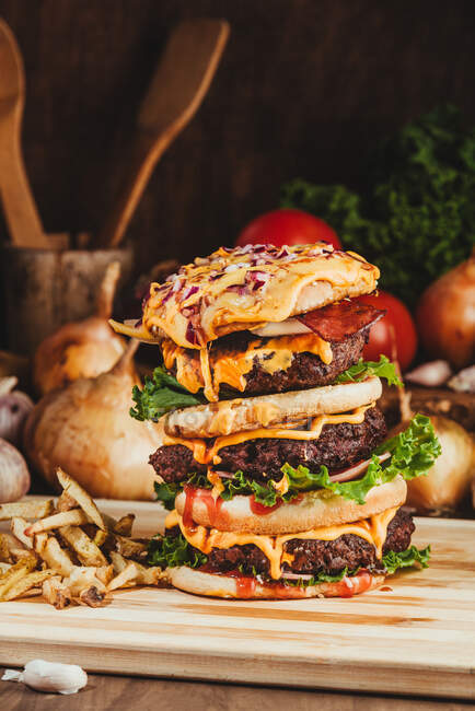 Hambúrgueres apetitosos com legumes colocados em tábua de madeira com batatas fritas na cozinha — Fotografia de Stock