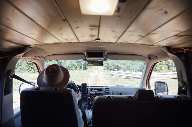 Back view of anonymous traveler riding van along road in woods during trip in summer — Stock Photo