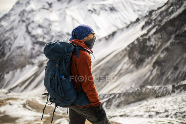 Боковой вид туриста-мужчины в теплой верхней одежде, стоящего на холме на фоне заснеженных Гималайских гор зимой в Непале — стоковое фото