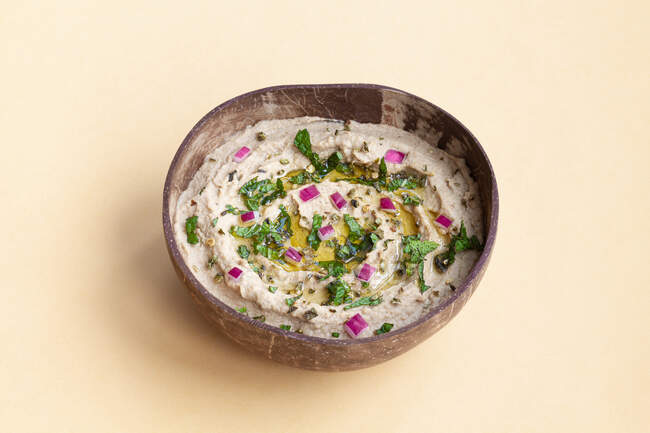 From above of appetizing traditional Baba ghanoush dish made of eggplants and garnished with herbs served in bowl on beige background — Stock Photo