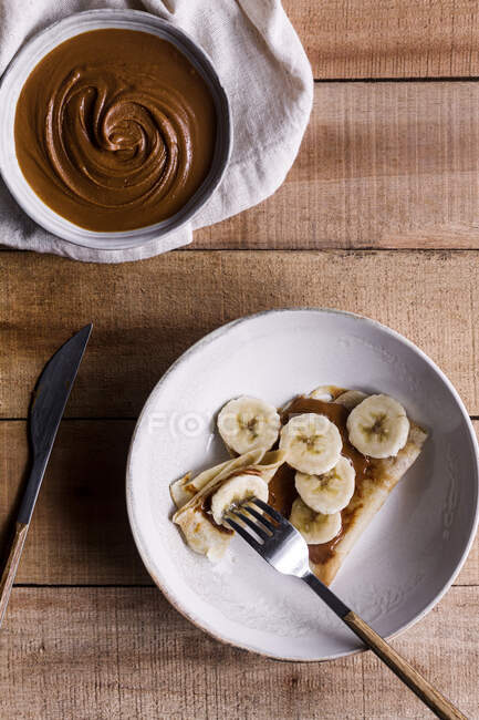 From above silverware placed near yummy crepes with sweet nut butter and slices of banana on wooden table — Stock Photo