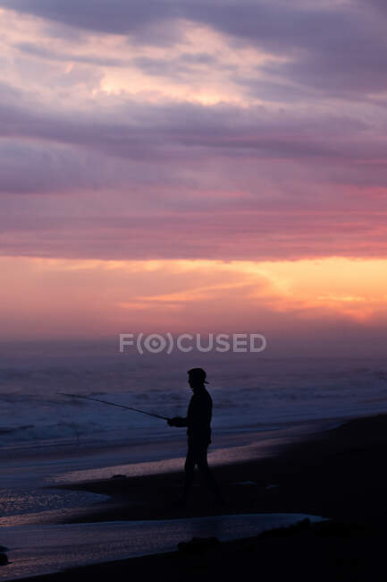 Силуэт человека, рыбачащего на берегу моря на закате — стоковое фото