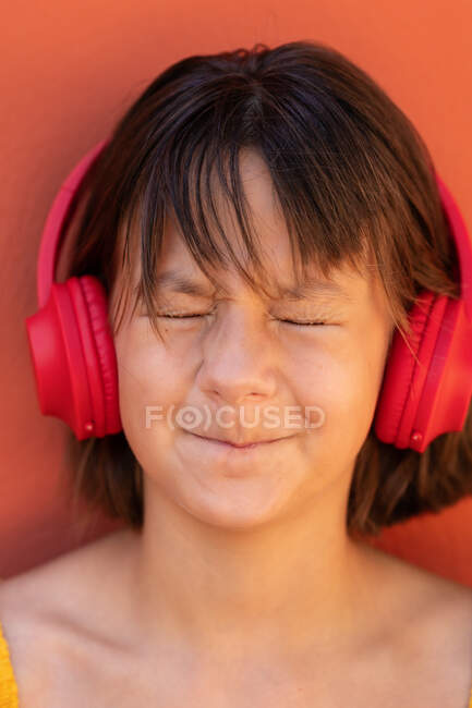Contenu enfant écoutant la chanson du casque sans fil sur fond orange — Photo de stock