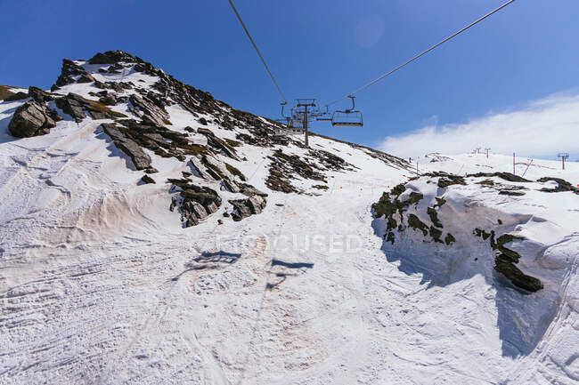 Ropeway with cabins over rough ridge with snow under cloudy blue sky in province of Granada Spain — Stock Photo