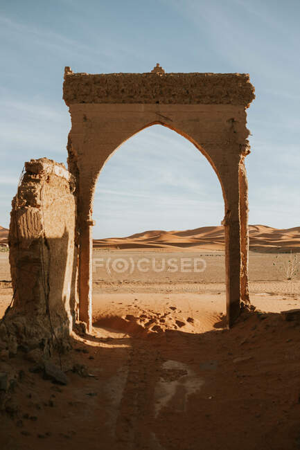 Bogen eines zerstörten alten Gebäudes in Sandwüste gegen wolkenverhangenen Himmel an einem sonnigen Tag in der Nähe von Marrakesch, Marokko — Stockfoto