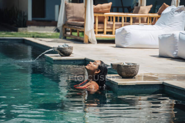 Vue latérale du touriste femelle avec les yeux fermés profitant dans la piscine ondulée contre bol avec liquide aqua en été — Photo de stock