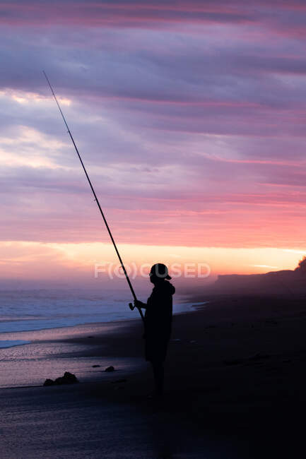 Silueta de un hombre pescando en la orilla del mar al atardecer - foto de stock