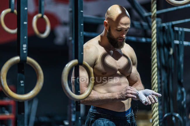 Muscular bearded guy in sportswear spreading powder during bodybuilding workout in gym — Stock Photo