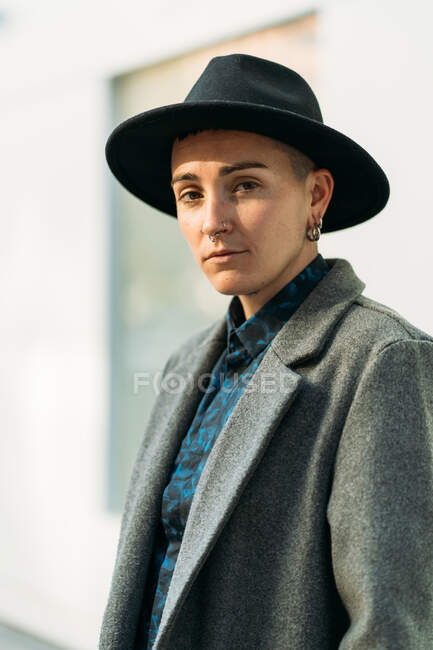Jeune transgenre en manteau et chapeau classe regardant la caméra en plein jour — Photo de stock