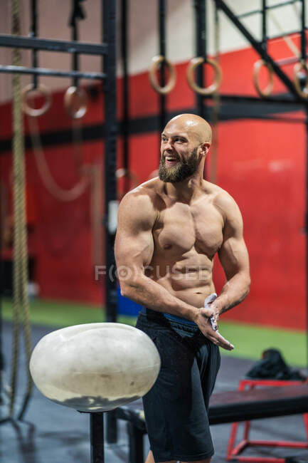 Homem barbudo muscular em sportswear palmas e espalhando pó durante o treino de musculação no ginásio — Fotografia de Stock