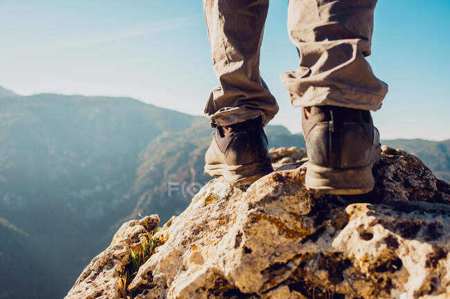 Unrecognizable crop explorer in trekking boots standing on rocky hill in highlands on sunny day — Stock Photo