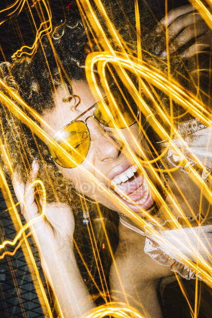 Senhora étnica jovem expressiva com cabelo afro em óculos de sol elegantes e cabeça tocando superior e gritando alto enquanto arrefece na boate perto de luzes congeladas — Fotografia de Stock